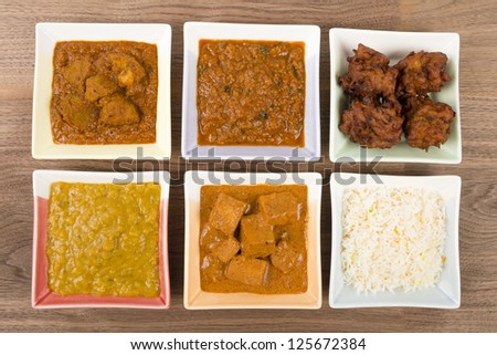 Thali - Indian meal set with vegetarian and meat curries, pilau rice and onion bhajis - pork vindaloo, keema madras, tarka dal and paneer makhani. Overhead shot.