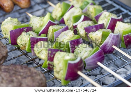 Lime, Mint & Coriander Chicken Kebabs - Chicken with red onion and green peppers on a skewer being cooked on a portable BBQ. Burgers and sausages around.