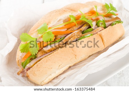 Banh Mi - Crusty bread filled with smoked duck breast slices, carrot and daikon radish pickle (do chua) and green chilies, garnished with coriander. Vietnamese sandwich.