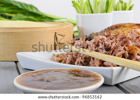Peking Duck - Chinese roast duck served with pancakes, cucumber, spring onions and hoisin / plum sauce. Close-up - Shallow depth of field and focus on chopsticks.