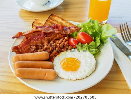 breakfast with fried eggs, bacon, sausages, beans, toasts and fresh salad
