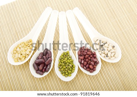 Various beans in various color in white spoon staked on wood pedestal.