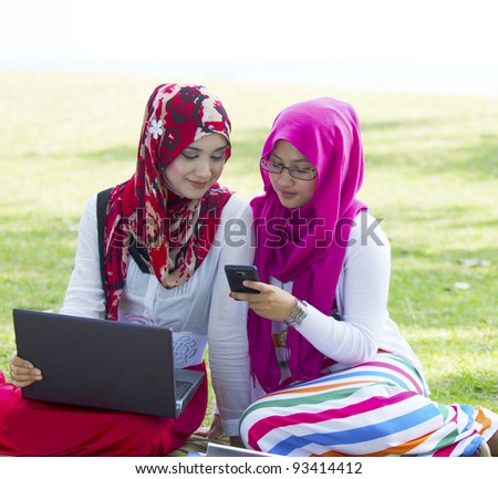 Two pretty Muslim lady in conversation while surfing internet using notebook and smartphone.