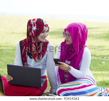 Two pretty young Muslim lady in conversation while shown something in smartphone.