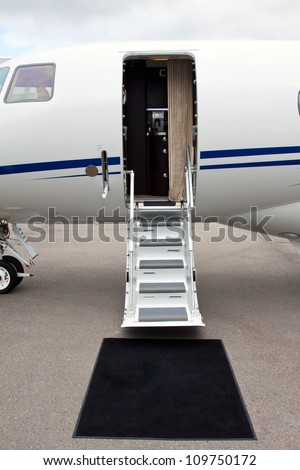 white private jet and open ladder, black carpet at the airport on a background cloudy sky