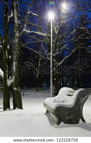 bench and snow in the light of a lantern at night