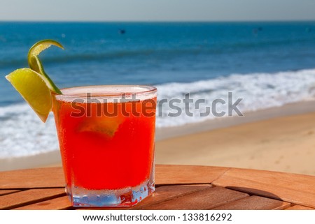 red alcohol cocktail on wooden table with crushed ice on background blue sky and sea