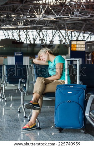 beautiful young woman with blond short hair with a suitcase sleep on a chair at the airport and waiting for her flight