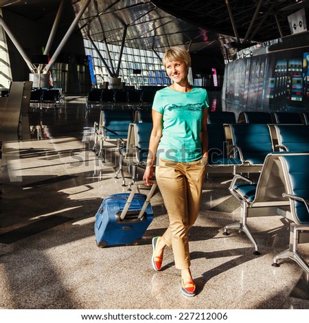 beautiful young woman with blond short hair with a suitcase at the airport and waiting for her flight