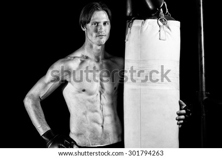 Young adult martial artist with heavy bag. Studio shot over black. Black and white.