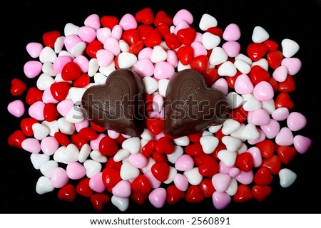 Two chocolate hearts on a bed of candy hearts.