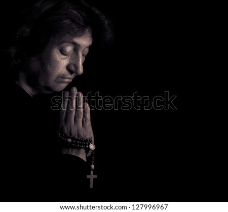 Senior Christian prays. Low-key lighting.
