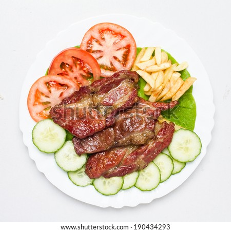 Beautifully grilled and slightly smoked pork cuts served o white plate with cucumbers, tomato and fries