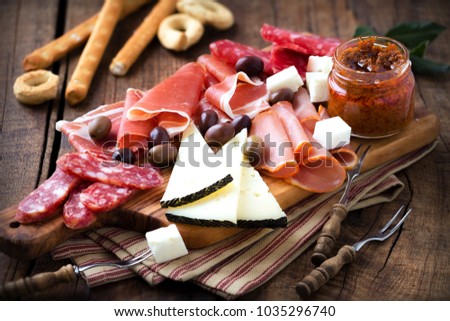 Cured meat and cheese platter of traditional Spanish tapas - chorizo, salsichon, jamon serrano, lomo and slices of goat cheese - served on wooden board with olives and bread sticks ストックフォト © 