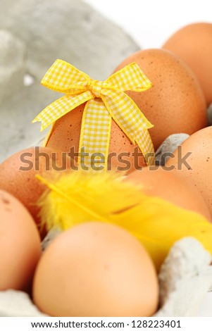 One Easter egg decorated with a yellow bow among other non decorated eggs in the carton packaging