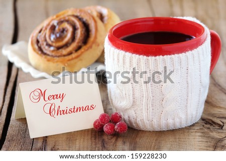 Cozy rustic Christmas setting - red mug of black coffee  in a white knitted cup holder with a wrapped gift and a greeting card