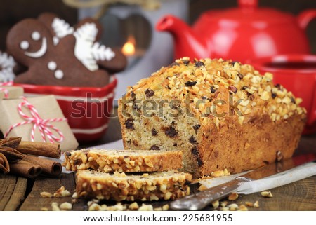 Cozy Christmas table setting with a freshly baked sliced festive cake with chocolate and chopped nuts, red teapot, gingerbread cookies, presents and a lantern with a lit candle at the background