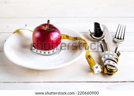 plate with apple measure tape, knife and fork. Diet food on wooden table
