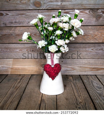 delicate bouquet of carnations in vintage vase with heart on wooden background. Valentine\'s Day