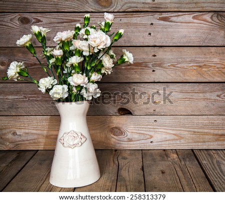 delicate bouquet of carnations in a vase on a vintage wooden background