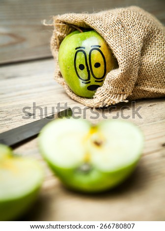 Knife slice apple on wooden background. Apple with painted face in shock