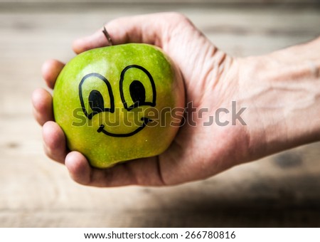 showing apple in hand on wooden background with a face on the apple , healthy food concept