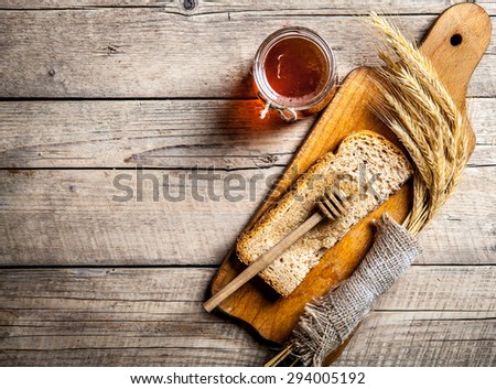 Honey in a jar, slice of bread, wheat and milk on an old vintage planked wood table from above. Rural or rustic style breakfast concept. Background layout with free text space.
