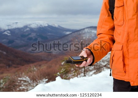 Close up of backpacker holding in his hand GPS navigator, Global Positioning System device. Mountain winter landscape as a background.