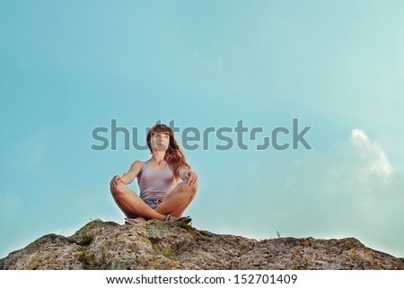 Portrait of a smiling young woman sitting on the top of mountain. Sky as background