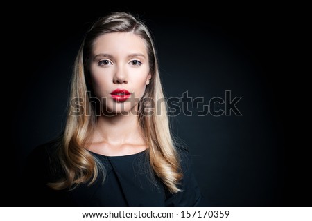 Studio portrait of a beautiful young woman in a black dress with long blonde hair, isolated on black background