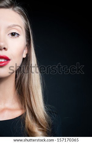 Close-up studio portrait of a half face of a beautiful young woman in a black dress, isolated on black background