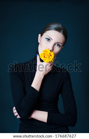 Portrait of beautiful woman with yellow rose flower in her mouth and blue make up and nails
