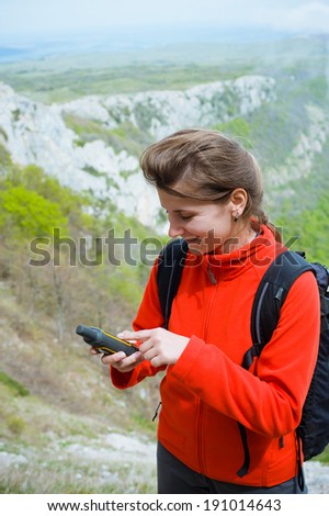 Portrait of a young woman tourist holding GPS navigator, Global Positioning System device. Mountain summer landscape as a background