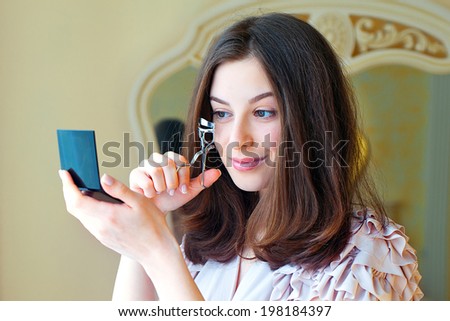 Portrait of  beautiful young woman looking at the mirror using eyelash curler