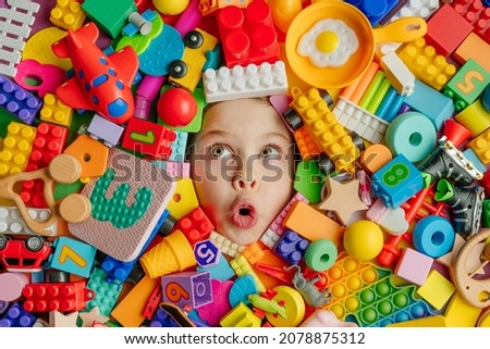Funny surprised little girl lying in the chaos of toys. Kid's face surrounded by building blocks. 商業照片 © 