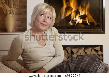 Daydreaming adult woman sitting on sofa at home by fireplace