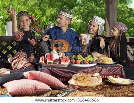 The head of the family playing mandolin during breakfast. Whole family dressed in Central Asian clothes
