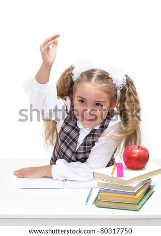 A young schoolgirl at a desk raises her hand to ask or answer a question