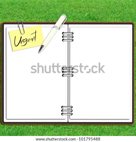 Paper note book leather cover with pen and sticky paper urgent text over grass