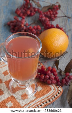 Tea made from frozen mountain ash and orange in a glass and mountain ash with orange on the table.