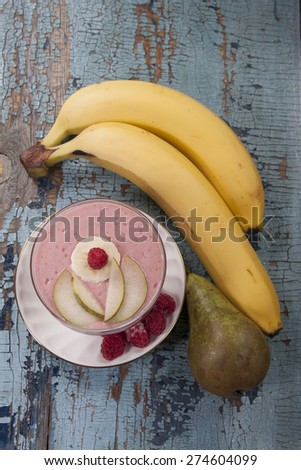 Smoothies of pear, banana and frozen raspberries with yogurt. Bananas and pears in the background on an old blue table.