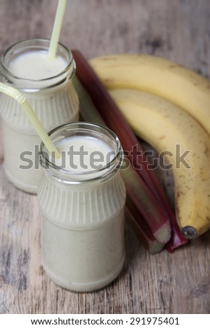 Smoothie of banana and rhubarb with yogurt in a glass. Bananas and rhubarb in the background on a wooden  table.