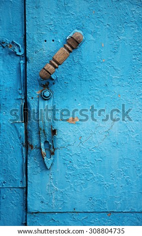 Detail of old door with handle. Old metal door covered with blue paint with cracelures.