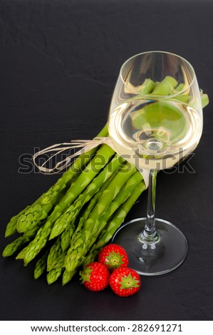 A bunch of fresh green Asparagus on Slate, with a glass of White Wine and Strawberries