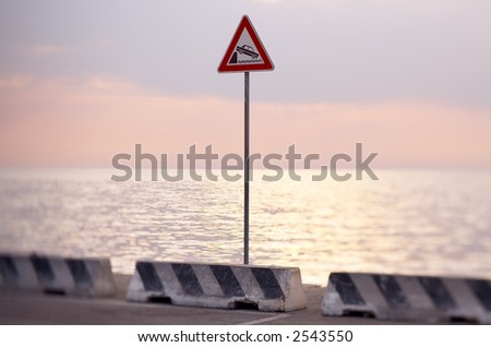 Danger warning sign on a city dock in front of a sunset lit sea