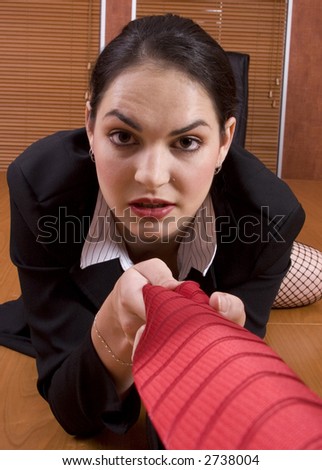 Brunette business woman with black suit crawling on desk holding red tie