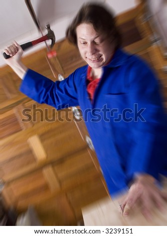 Dark haired man with blue overall holding hammer about to hit nail