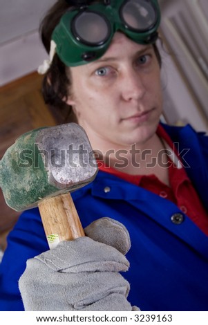 Dark haired man with blue overall holding hammer (focus on the hammer)