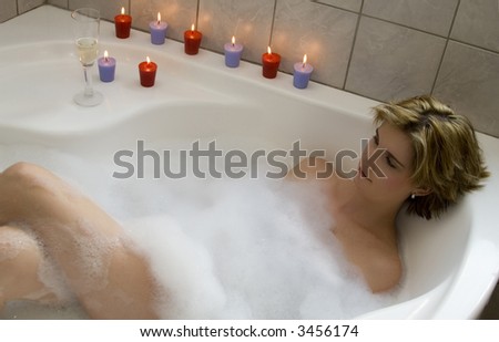 Attractive blond woman lying in bubble bath with several candles and champagne