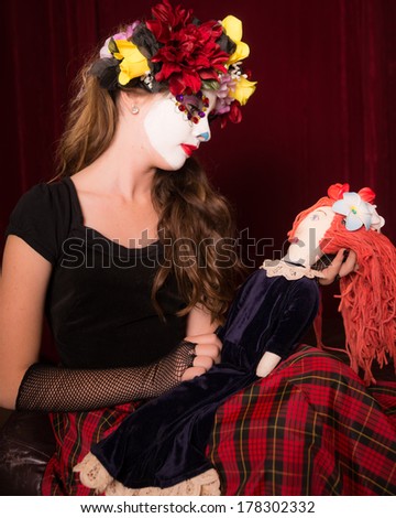 Day of The Dead girl in make up, costume, and headress holding creepy doll